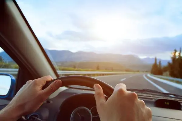 Hands of a driver on steering wheel of a car and empty asphalt road