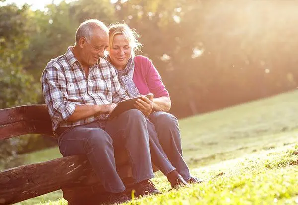 senior man and woman sitting on a bench looking at a mobile-friendly website on a tablet