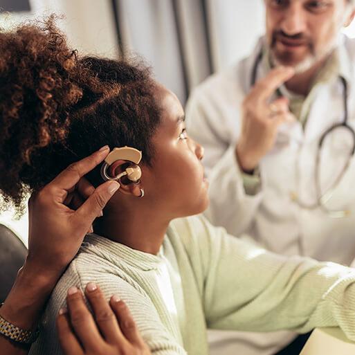 Smiling deaf girl with ear implant at doctor's office.