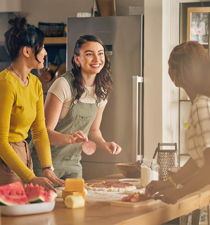 Happy, friends and women cooking pizza in kitchen, bonding and having fun together in home.