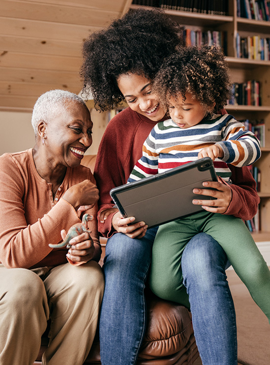 Grandmother, mother, and toddler sitting together looking at a tablet