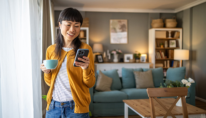 woman checking her phone while standing holding a cup of coffee