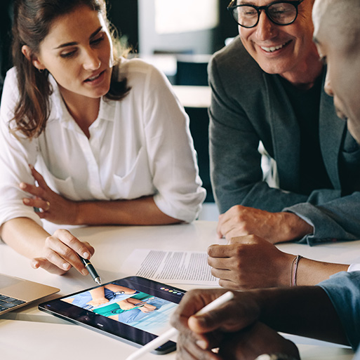 three people sitting around a table looking at an image on a tablet