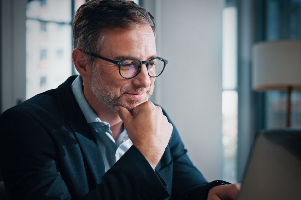 Healthcare executive in glasses thoughtfully reviewing data on a laptop.